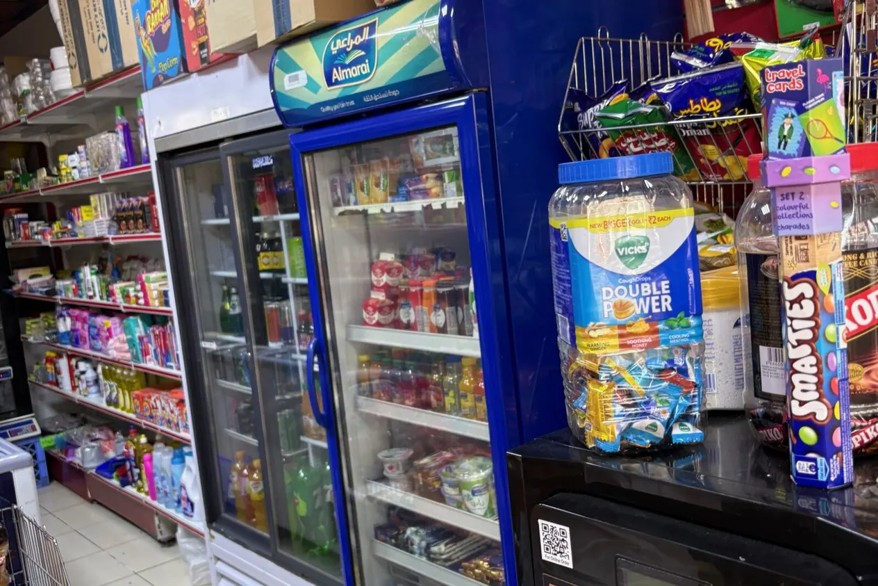 A neighbourhood grocery shop (bakkala) in the UAE, its shelves and fridge stocked with drinks, snacks and fresh produce.